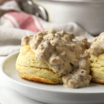 A fluffy buttermilk biscuit smothered in sausage gravy on a white plate.