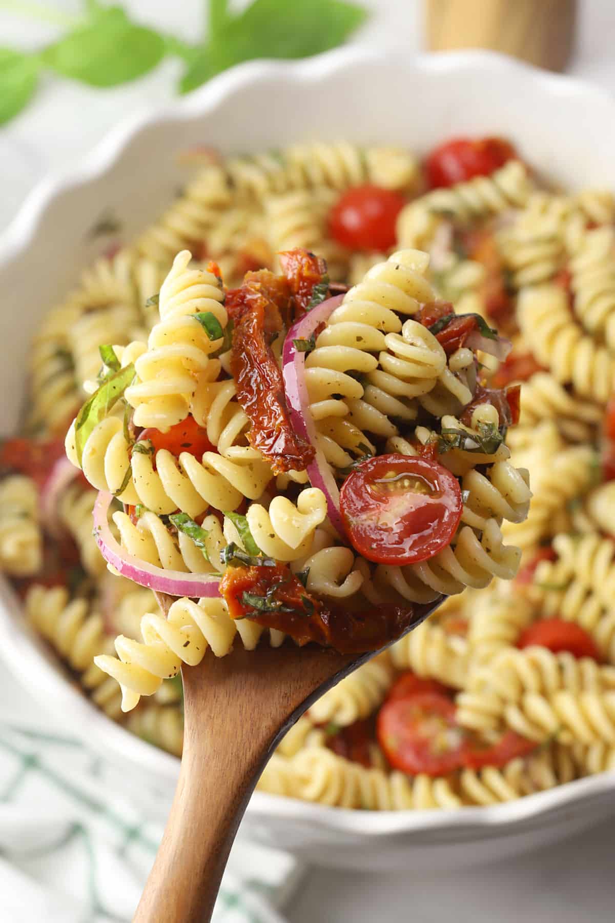 A wooden serving spoon filled with sun-dried tomato pasta salad.