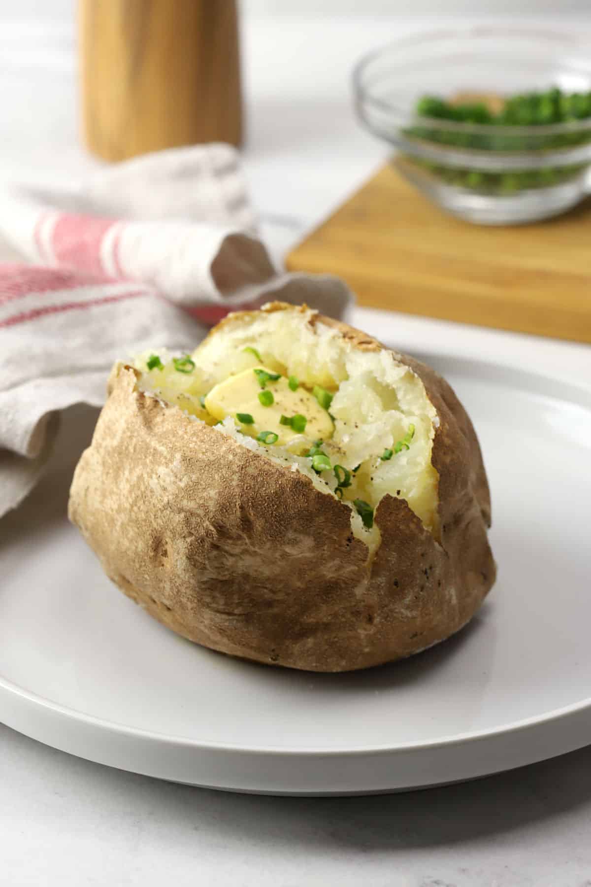 A baked potato on a white plate topped with butter and chives.