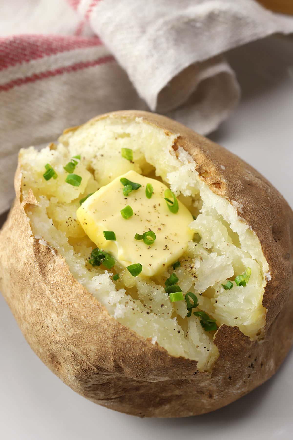 Close up of a fluffy baked potato with butter and chives.