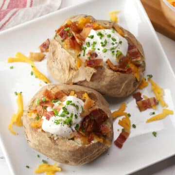 Two loaded baked potatoes on a square white plate.
