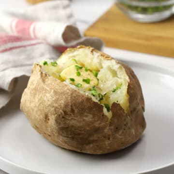 A baked potato on a white plate topped with butter and chives.