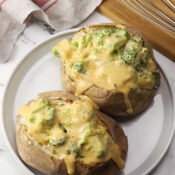 Two baked potatoes topped with broccoli cheese sauce on a white plate.