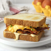 A prepared bacon, egg, and cheese sandwich with dripping sauce on a white plate.