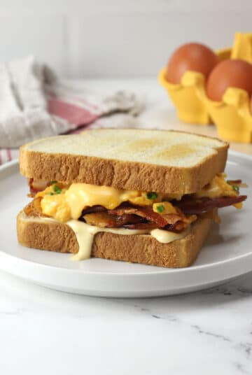 A prepared bacon, egg, and cheese sandwich with dripping sauce on a white plate.