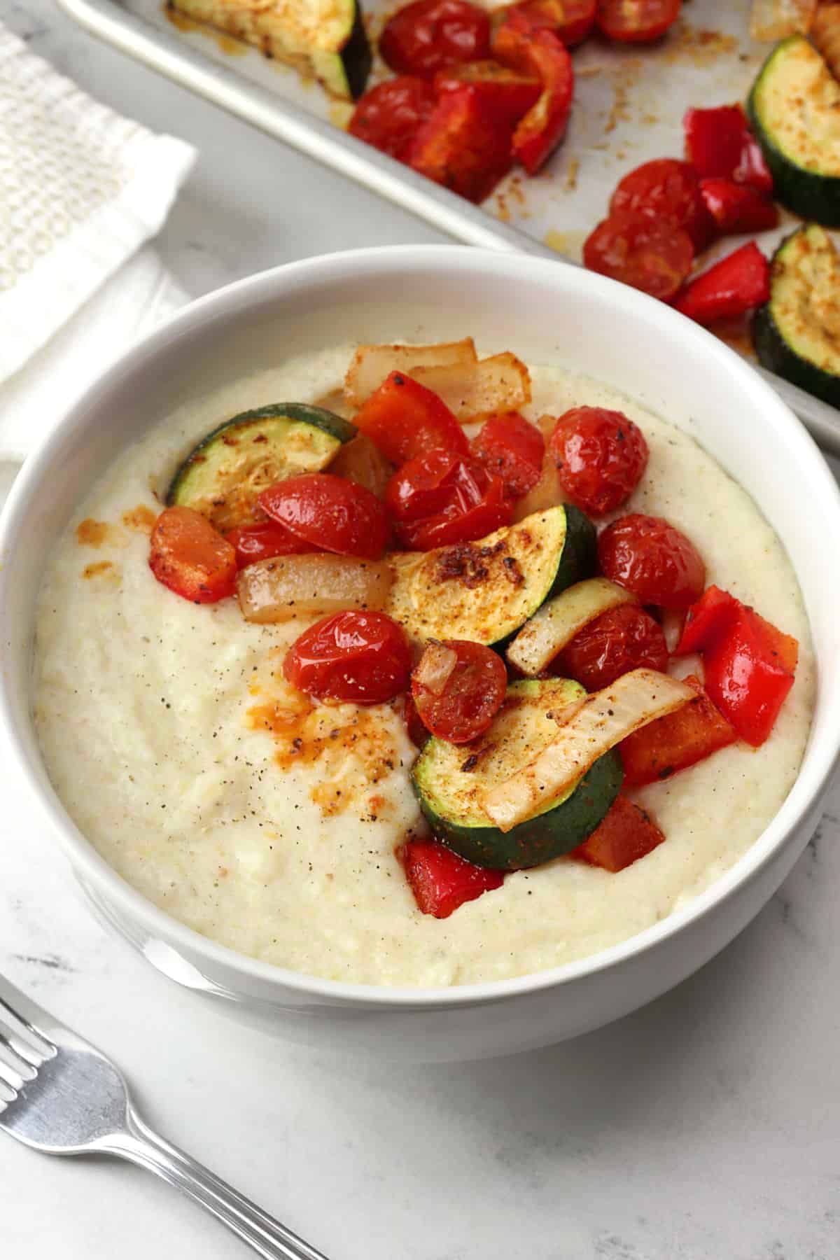 A white bowl filled with creamy grits topped with roasted vegetables.