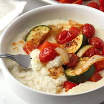 A fork in a bowl of creamy grits and roasted vegetables.