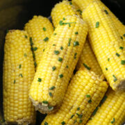 Crock pot bowl filled with con on the cob topped with chives.