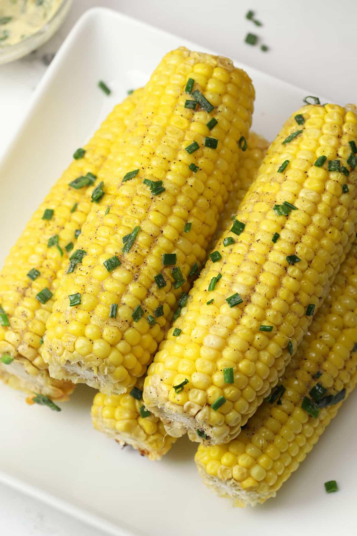 Cooked corn on the cob stacked on a white serving plate.