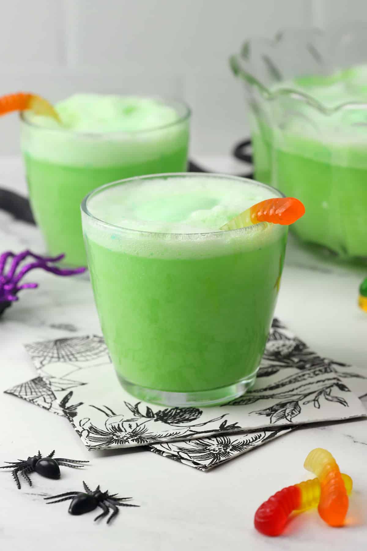Close up of a glass of green Halloween punch with a gummy worm garnish.