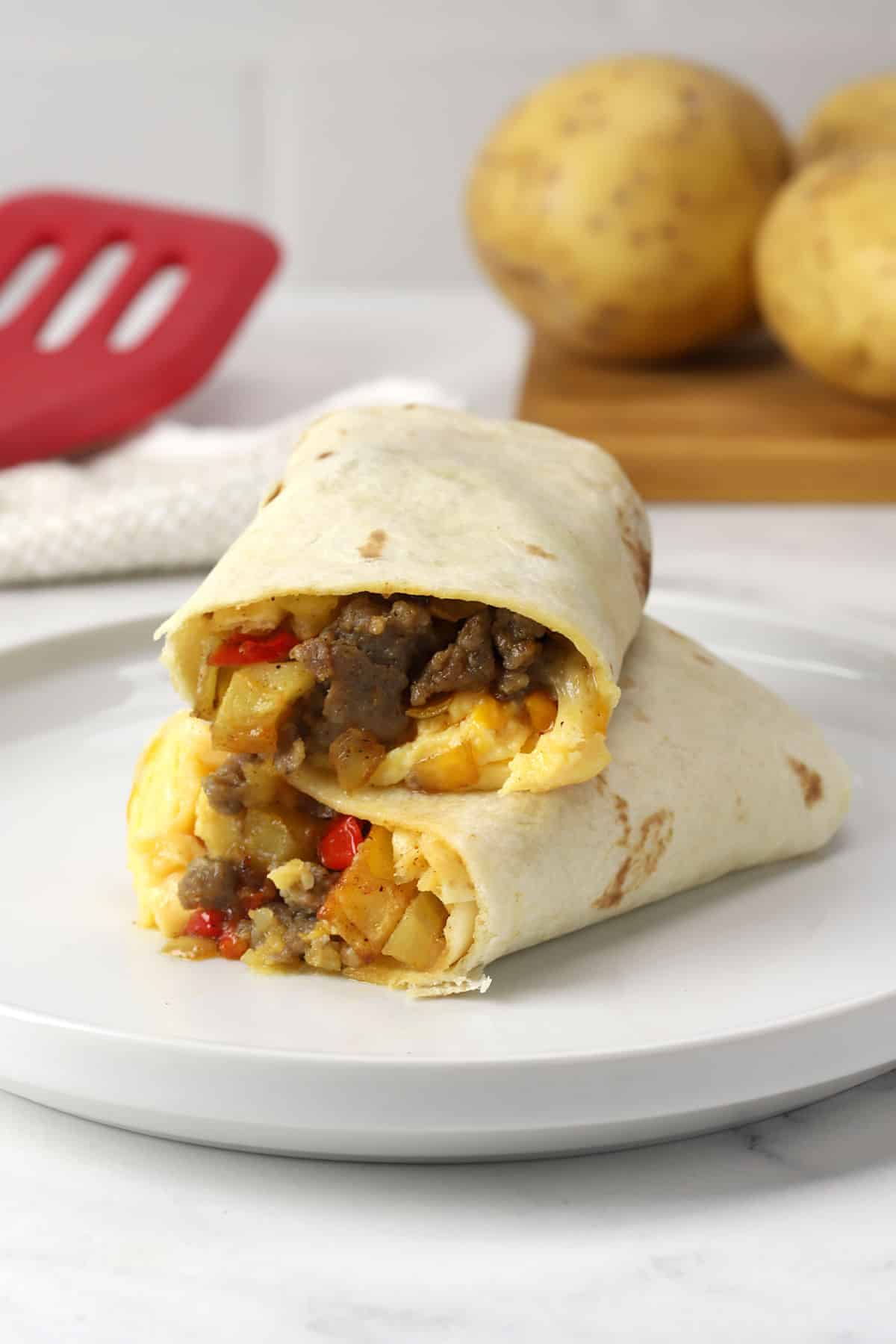 Two halves of a breakfast burrito with potatoes on a white plate.