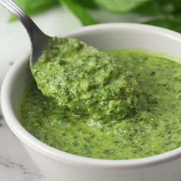A spoon scooping pesto from a white bowl.