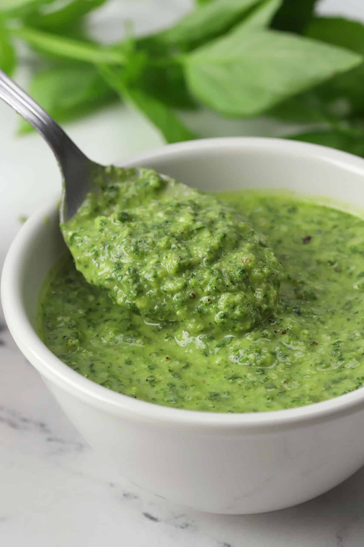 A spoon scooping pesto from a white bowl.