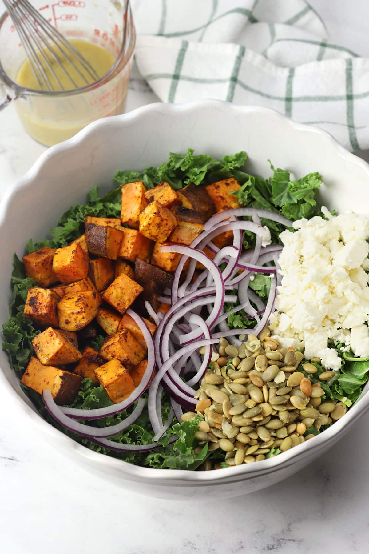 Sweet potatoes, feta cheese, onions, and pepitas on a bed of kale in a bowl.