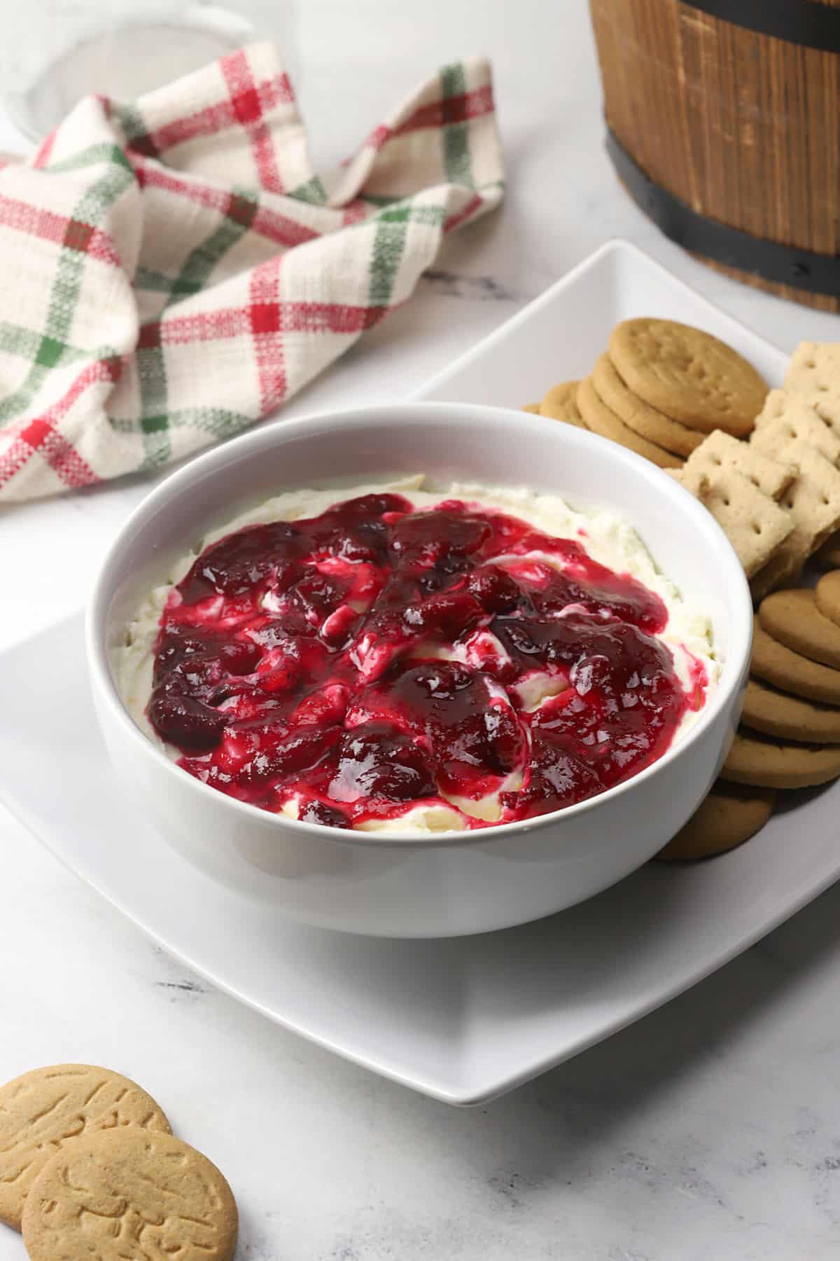 A white bowl filled with cheesecake dip topped with cranberry sauce.