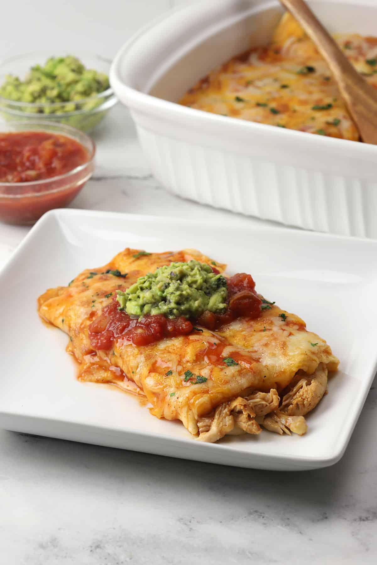 Two chicken enchiladas on a white diner plate topped with salsa and guacamole.