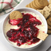 A bowl of cranberry cheesecake dip with ginger snap cookies and graham crackers.