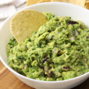 A bowl of guacamole with a tortilla chip.