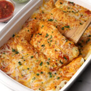 Enchiladas covered in melted cheese in a white casserole dish.