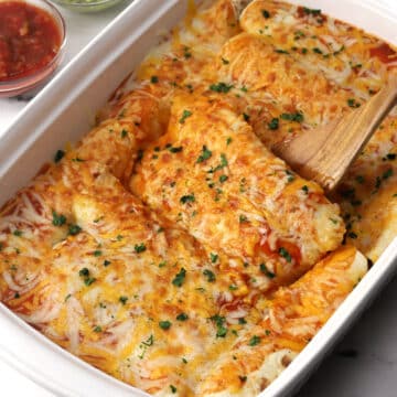 Enchiladas covered in melted cheese in a white casserole dish.