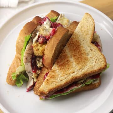 A turkey cranberry sandwich sliced in half on a white plate.