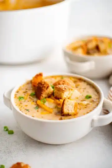 A white cup of cheeseburger soup topped with croutons.
