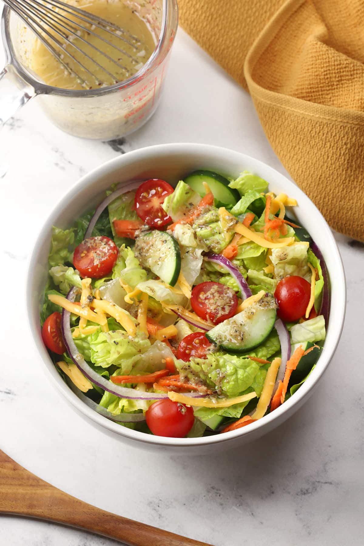 A white salad bowl filled with a serving of garden salad topped with dressing.
