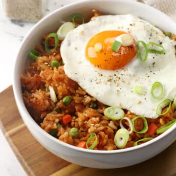 Close up of gochujang fried rice in a white bowl topped with a fried egg and green onions.