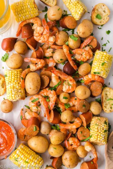 A spread of shrimp boil on a white cloth with butter and cocktail sauce.