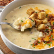 Close up of spoon in a bowl of potato soup topped with croutons and bacon.