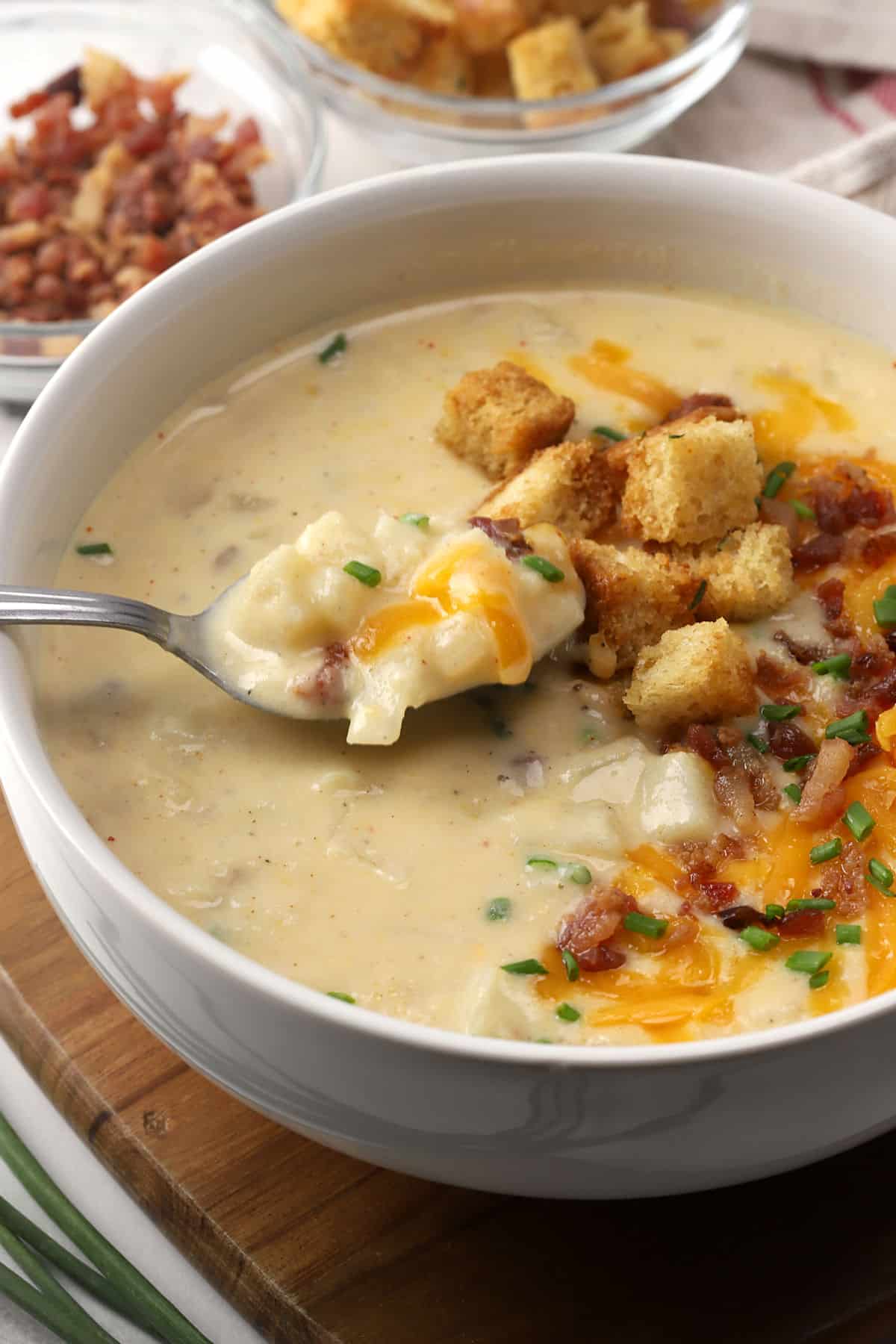 Close up of spoon in a bowl of potato soup topped with croutons and bacon.