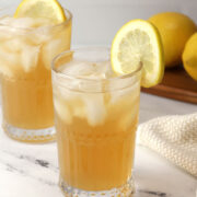 A glass of Arnold Palmer filled with ice and a lemon slice on the rim.