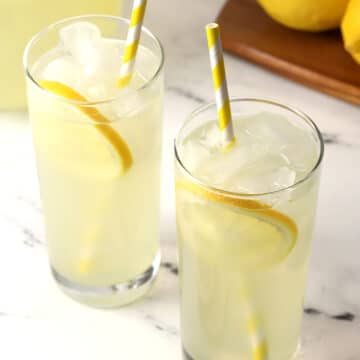 Close up of two glasses of lemonade with lemon slices and yellow striped straws.