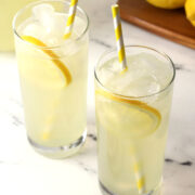 Close up of two glasses of lemonade with lemon slices and yellow striped straws.