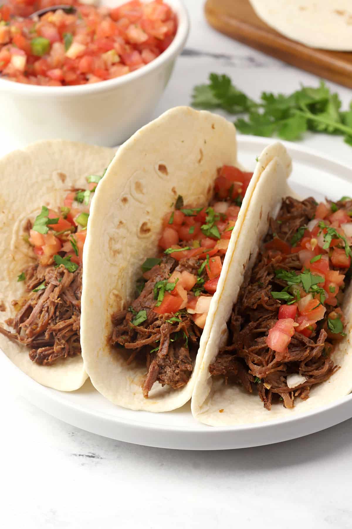 Three tacos made with flour tortillas filled with shredded beef and pico de gallo.