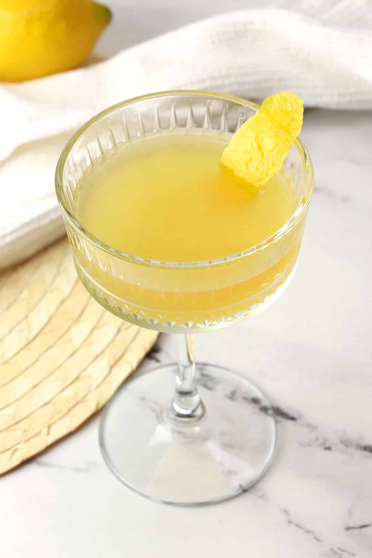 Close up of a bee's knees cocktail in a coupe glass with a lemon peel garnish.