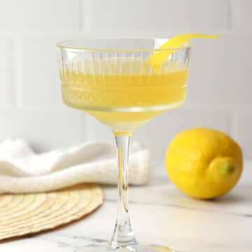 A coupe glass filled with bee's knees cocktail with a lemon peel garnish.