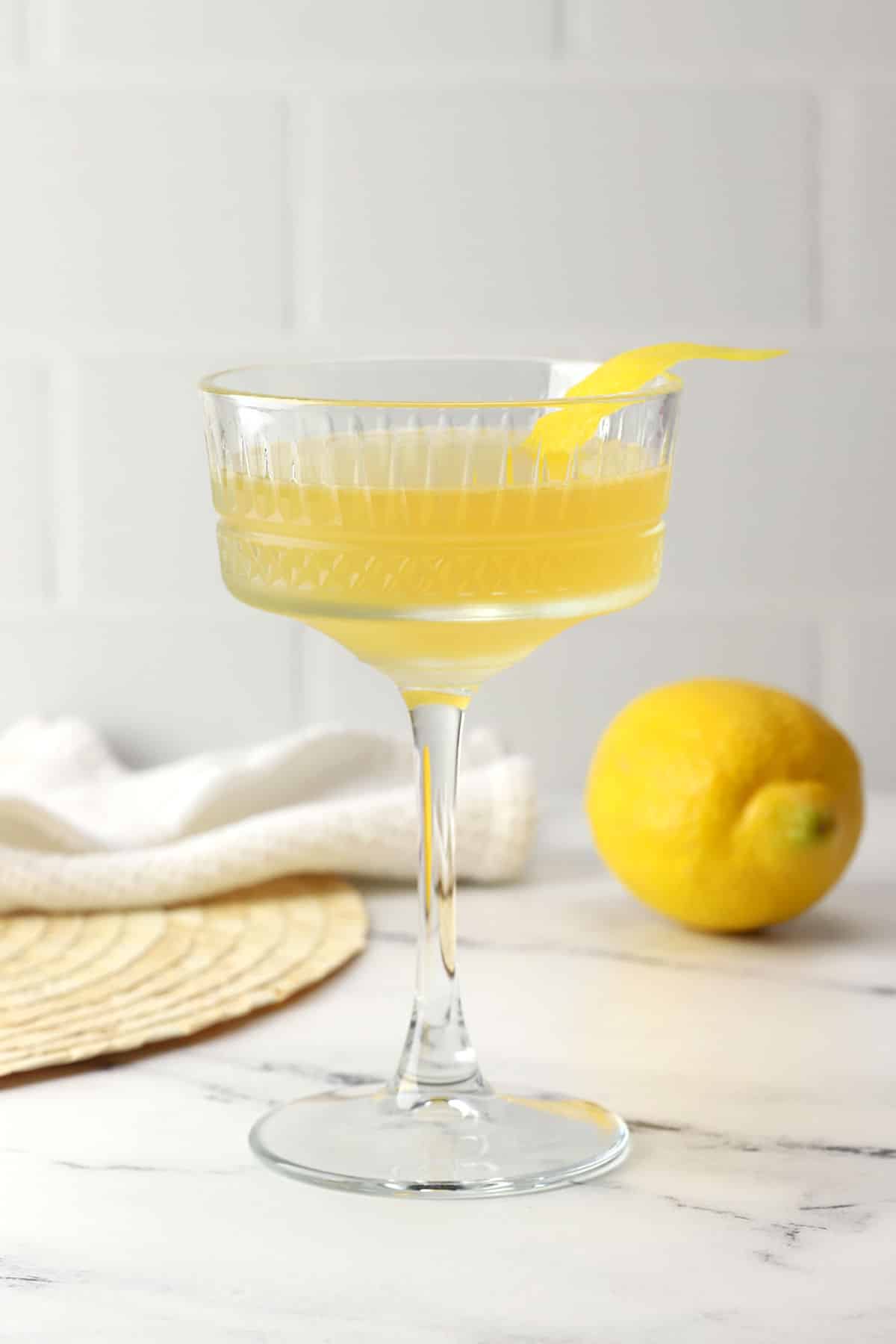 A coupe glass filled with bee's knees cocktail with a lemon peel garnish.