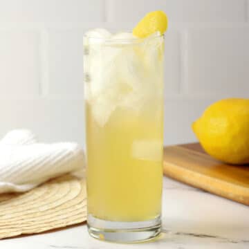 A highball glass filled with bee's knees spritz with a lemon peel garnish.