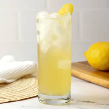 A highball glass filled with bee's knees spritz with a lemon peel garnish.