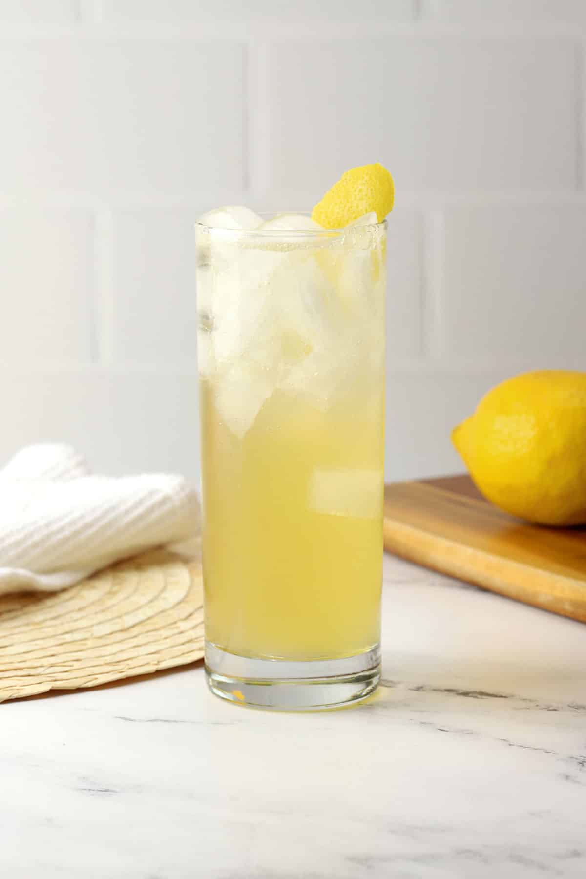 A highball glass filled with bee's knees spritz with a lemon peel garnish. 