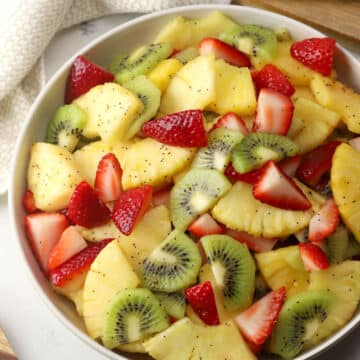 A bowl filled with spring fruit salad topped with poppy seed dressing.