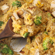 A wooden spoon scooping cheesy chicken broccoli rice from a sauté pan.