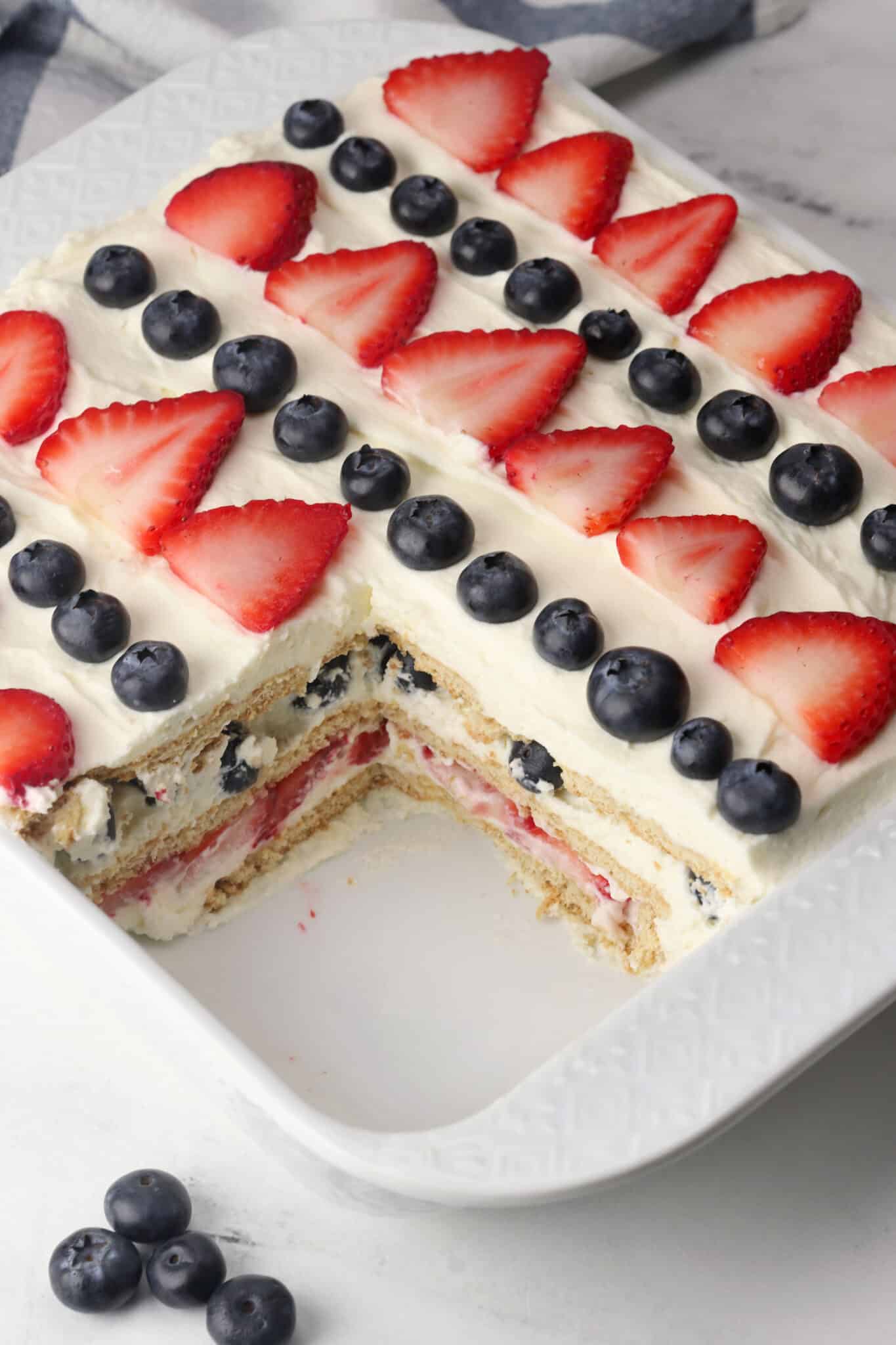 An icebox cake in a casserole dish that's topped with berries with a piece missing.