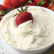 A strawberry in a bowl of cream cheese fruit dip.