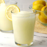 A glass filled with lemonade slushie with a lemon round garnish.