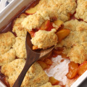Peach cobbler scooped from a casserole dish with a wooden serving spoon.