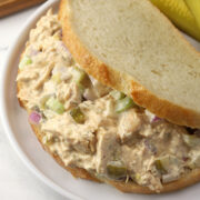 Closeup of a dill pickle chicken salad sandwich on a plate with pickle spears.