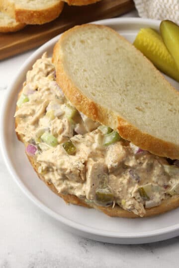 Closeup of a dill pickle chicken salad sandwich on a plate with pickle spears.