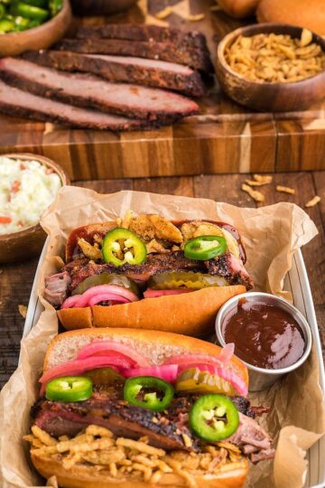 Two smoked brisket sandwiches on a serving tray with barbecue sauce.
